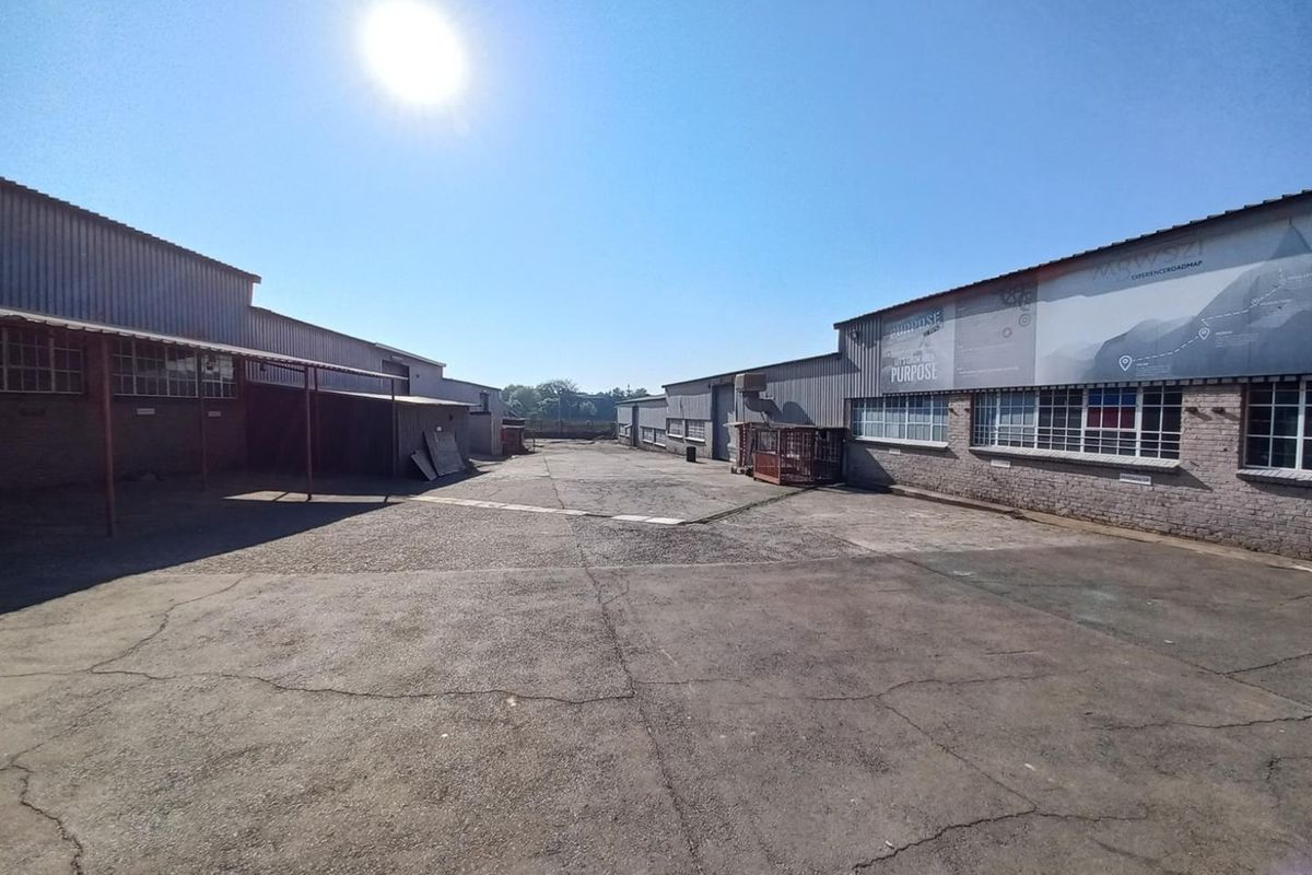 Spacious industrial yard area situated between two warehouse buildings, featuring concrete paving and covered loading or storage sections.