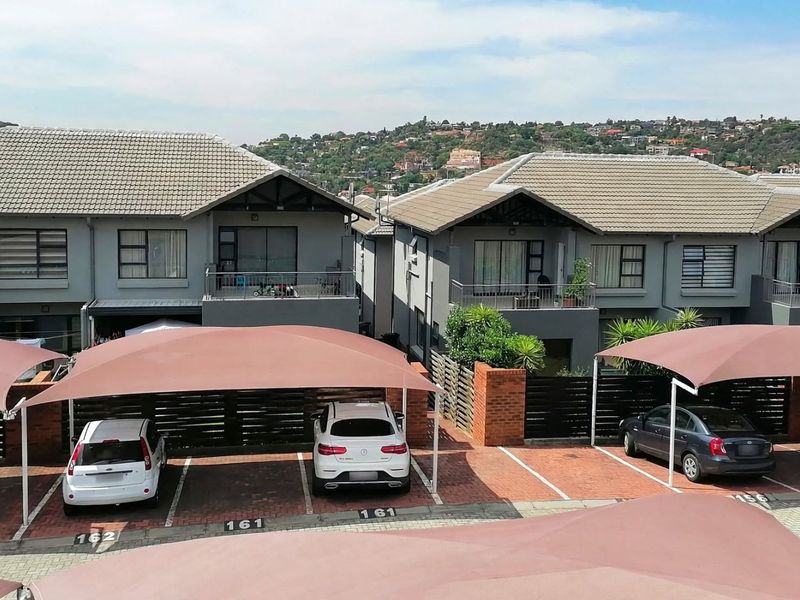 Elevated view of a townhouse complex featuring paved parking areas with shade cloth carports and multi-story residential units with balconies.