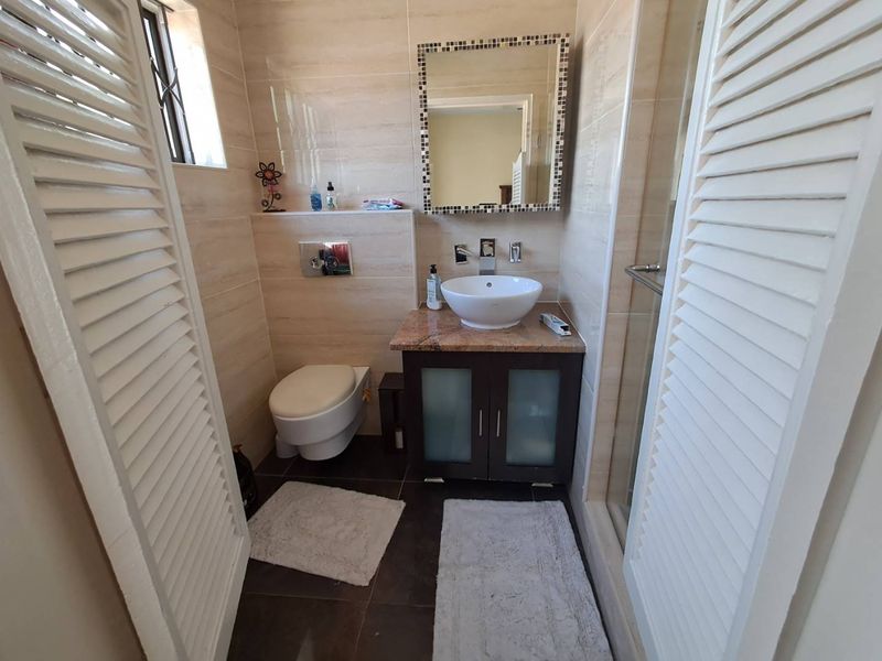 A compact, modern bathroom featuring a wall-mounted toilet, vessel sink with granite vanity, and a glass-enclosed shower with neutral wall tiling.