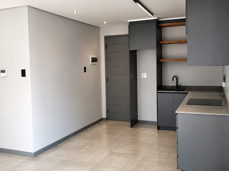 Modern open-plan kitchen featuring sleek dark cabinetry, stone countertops, integrated sink, and tiled flooring in a clean, contemporary apartment setting.