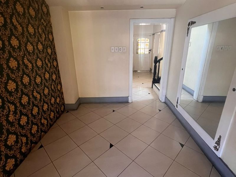 A spacious hallway featuring tiled flooring, decorative accent wallpaper, and a large built-in mirror, leading towards the main entrance area.