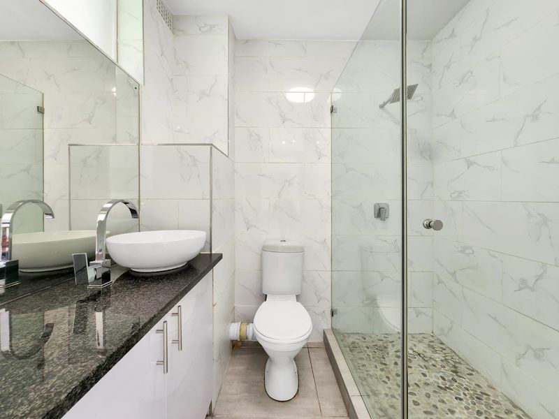 Modern bathroom featuring a glass-enclosed shower with pebble flooring, a granite-topped vanity with a vessel sink, and marble-look wall tiling.