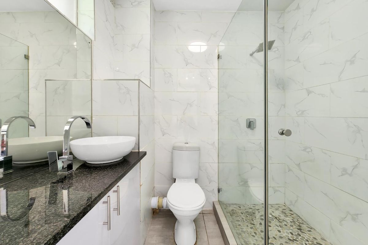 Modern bathroom featuring a glass-enclosed shower with pebble flooring, a granite-topped vanity with a vessel sink, and marble-look wall tiling.