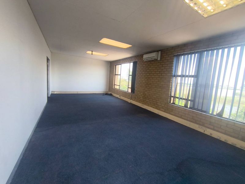 An empty, open-plan office space featuring exposed brick walls, recessed lighting, split-system air conditioning, and large windows with vertical blinds.