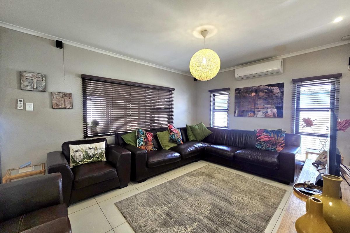 A comfortable living room featuring tiled flooring, venetian blinds, and a wall-mounted air conditioning unit.