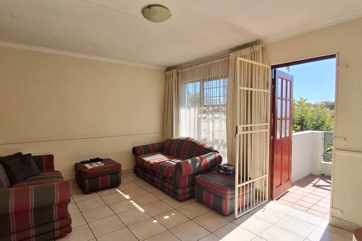 A living room featuring tiled flooring and direct access to an outdoor balcony through a security gate and door.