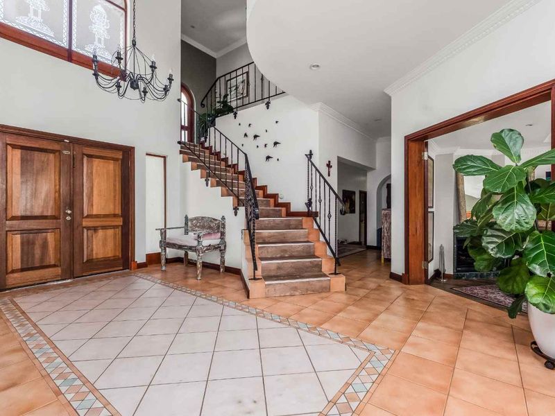 Spacious double-volume entrance hall featuring a grand staircase with wrought iron balustrades and elegant tiled flooring.