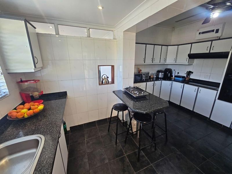 Functional kitchen featuring granite countertops, white cabinetry, a gas hob with extractor fan, and dark tiled flooring.