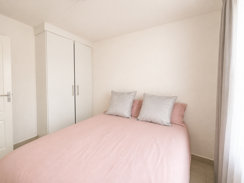 A bright bedroom featuring neutral walls, tiled flooring, and a functional built-in wardrobe.