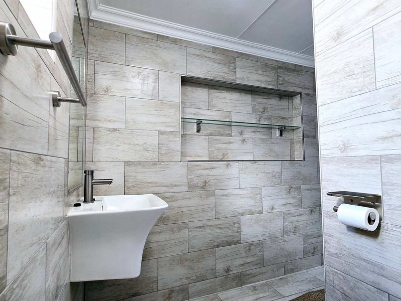 Modern bathroom featuring wood-look ceramic wall tiles, a sleek wall-mounted basin with mixer tap, and a convenient recessed storage niche with glass shelving.