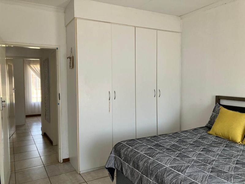 A bedroom featuring built-in white wardrobes and tiled flooring, with a view leading into the hallway.