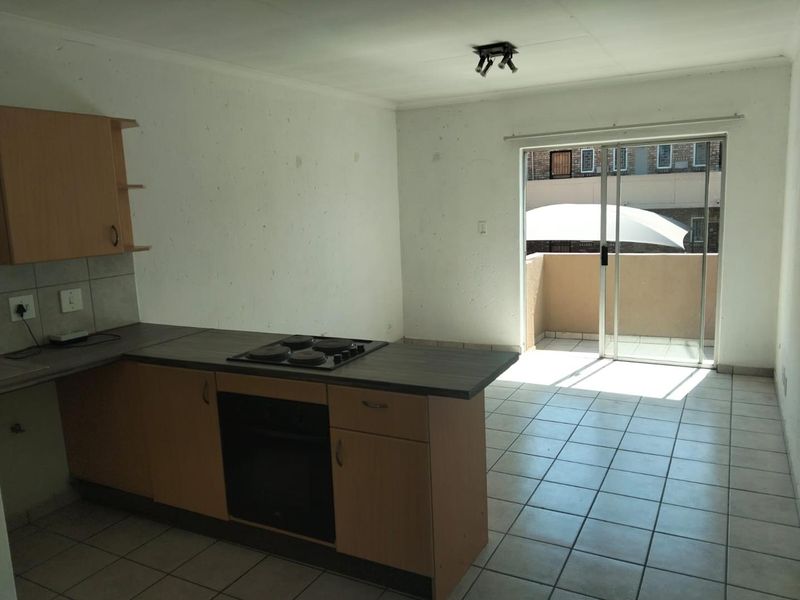 Open-plan kitchen and living area featuring tiled floors, built-in cabinetry with integrated oven and hob, and direct access to a private balcony.