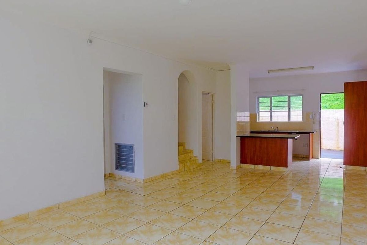 Open plan living and kitchen area featuring ceramic tiled flooring, built-in kitchen cabinetry, and an archway leading to the staircase.