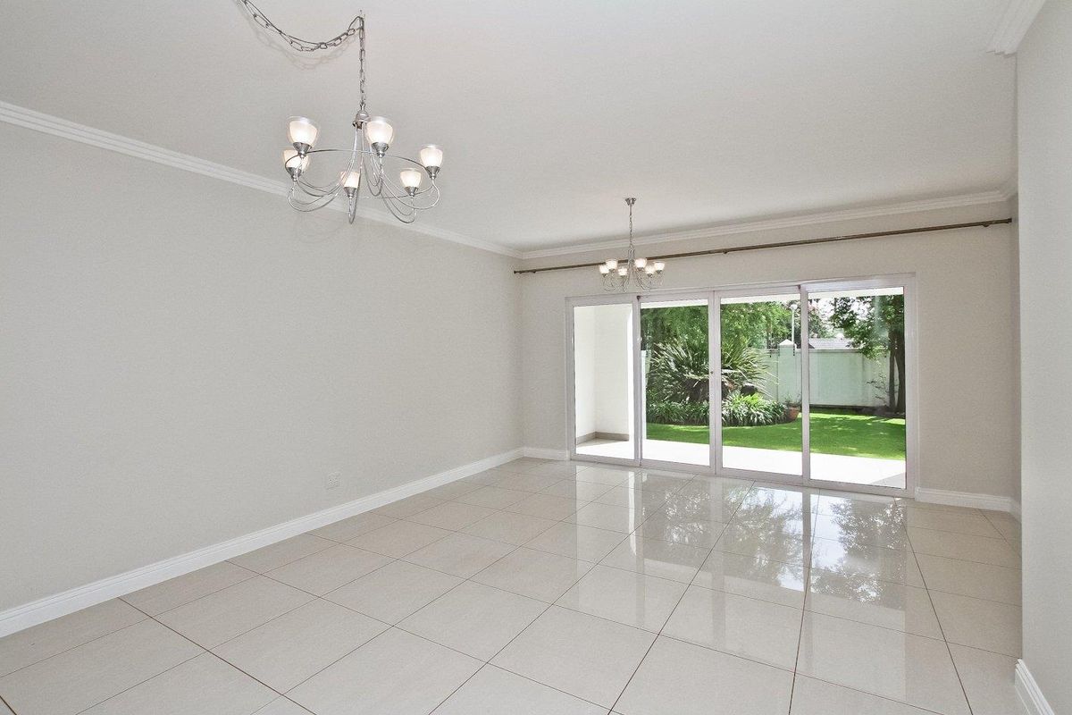 Spacious, light-filled living area featuring polished porcelain tile flooring, crown molding, and large sliding glass doors opening to a private garden.