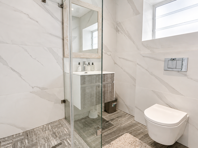 Modern bathroom featuring a wall-mounted toilet with concealed cistern, glass shower enclosure, and a contemporary vanity unit with marble-look wall tiling.