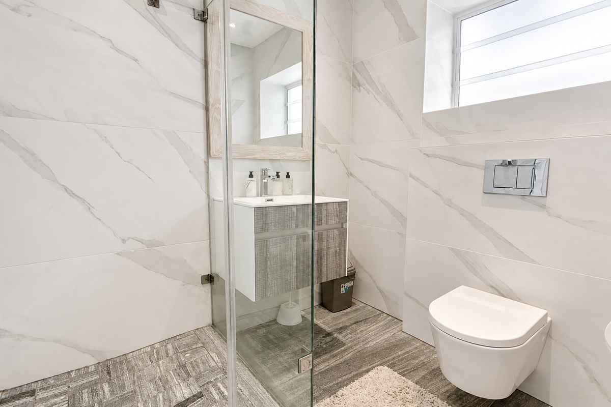 Modern bathroom featuring a wall-mounted toilet with concealed cistern, glass shower enclosure, and a contemporary vanity unit with marble-look wall tiling.