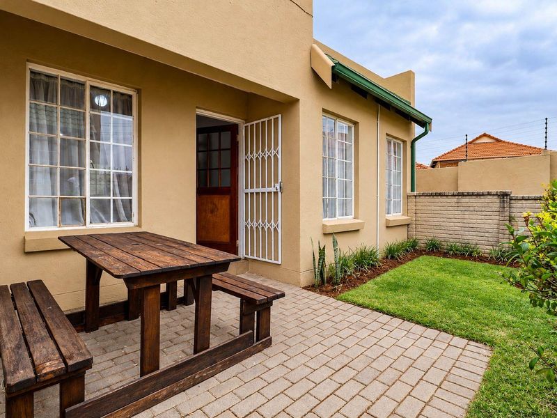 A private rear garden featuring a paved patio area, lawn, and secure boundary wall with electric fencing.