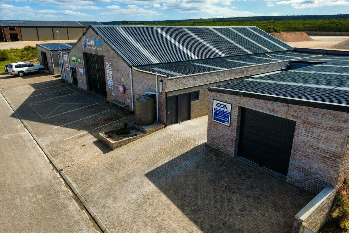 Aerial view of a commercial industrial property featuring brick construction, corrugated metal roofing, roller shutter doors, and a paved parking area.
