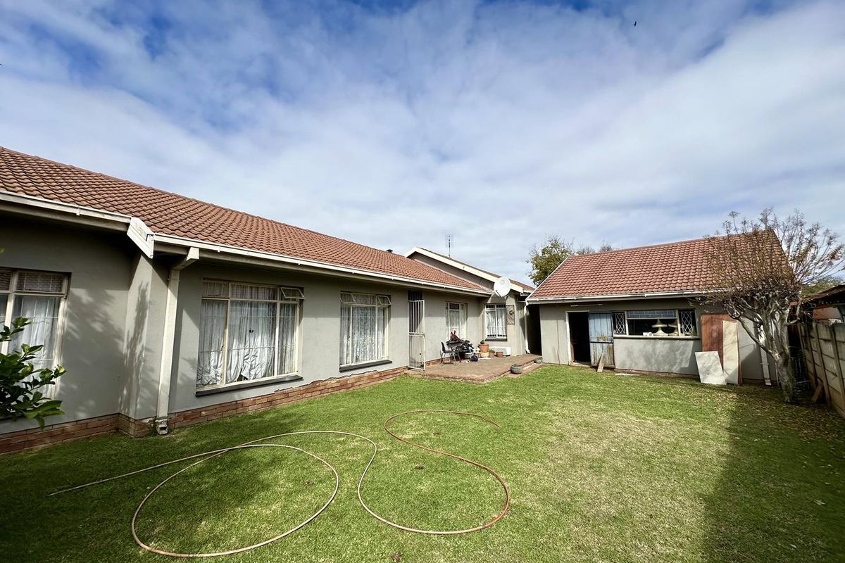 Rear view of the property featuring a lawn, paved patio area, and detached garage structure with tiled roofing.