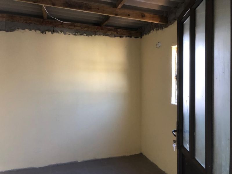 An unfinished interior room featuring exposed timber ceiling beams, a glass panel door, and a casement window, requiring final plastering and ceiling installation.