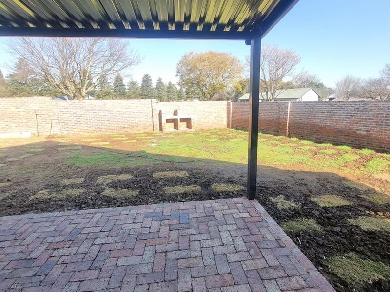 Covered patio area featuring brick paving, a built-in braai, and a spacious backyard enclosed by perimeter brick walls.