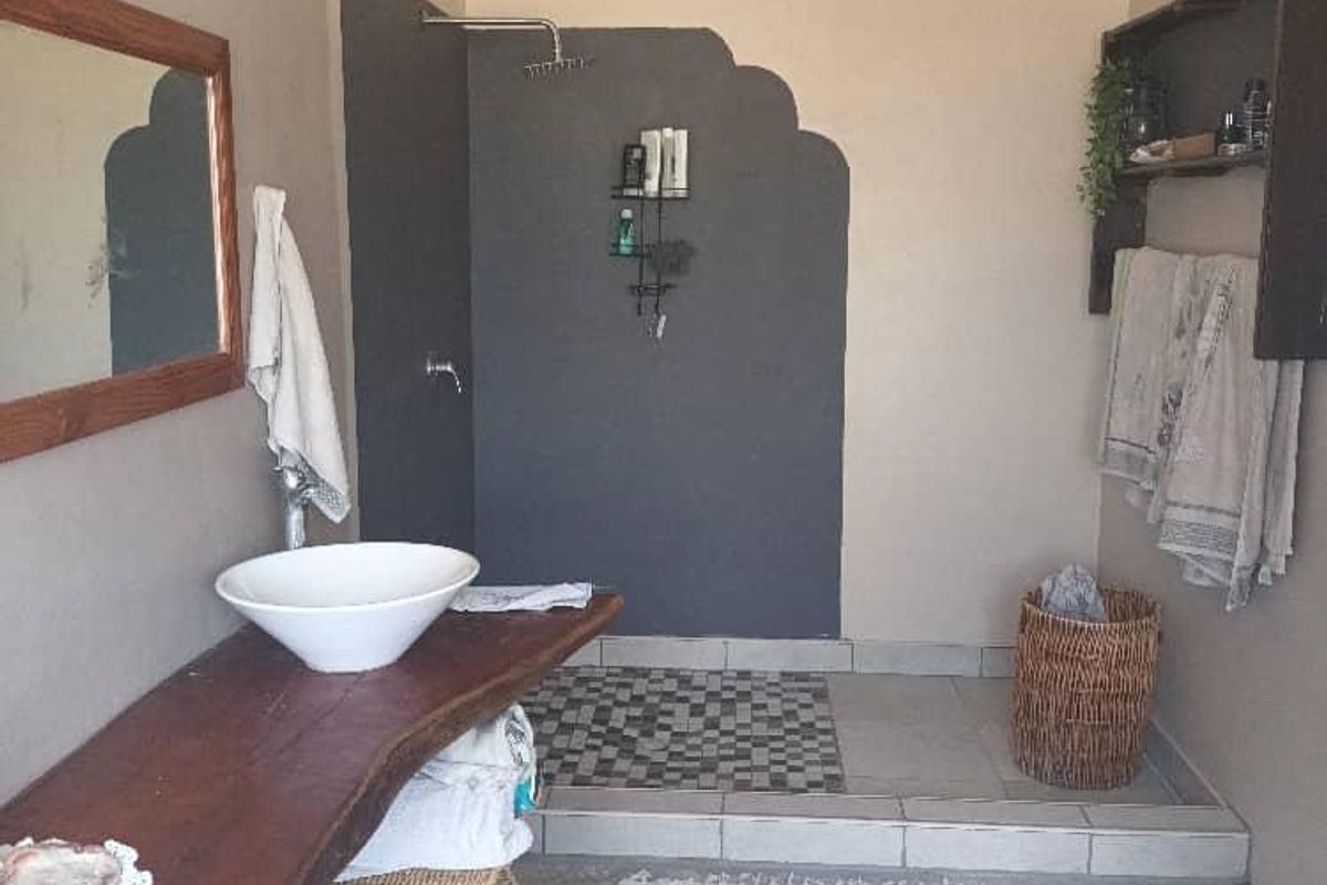 A bathroom featuring a vessel sink on a rustic wooden vanity shelf and a walk-in shower area with a tiled base.