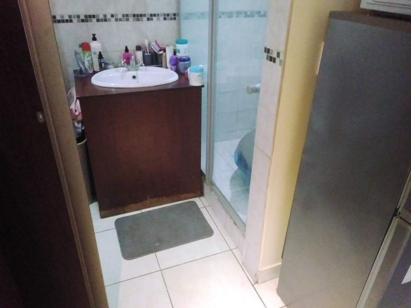 A compact bathroom featuring a vanity cabinet with a basin and a glass-enclosed shower, finished with tiled walls and flooring.