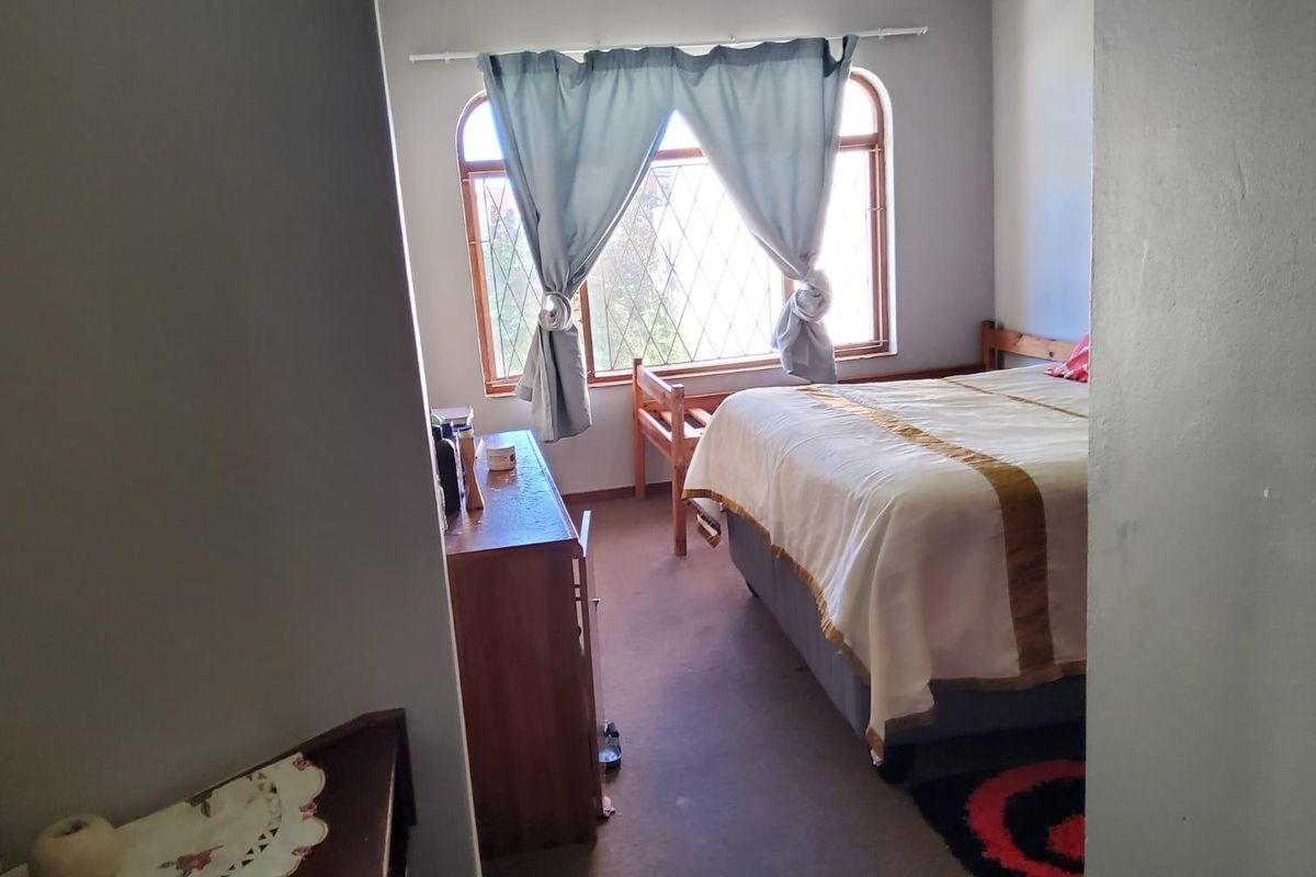 A bedroom featuring a large arched window with leaded glass detailing and carpeted flooring.