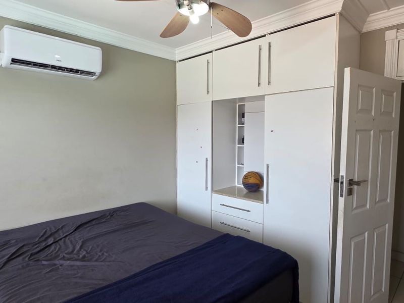 Bedroom featuring built-in white cabinetry, a ceiling fan, and a wall-mounted air conditioning unit.