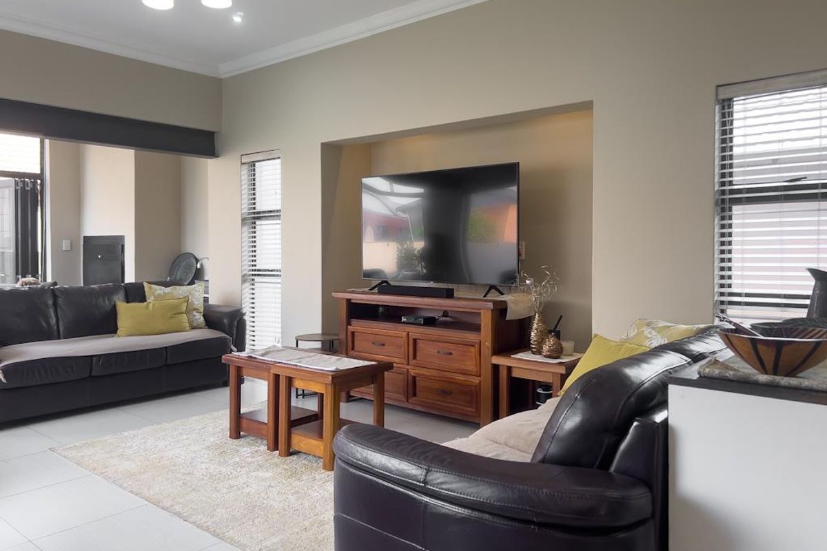 Spacious living room featuring a built-in media alcove, tiled flooring, and large windows with fitted blinds, creating a bright and comfortable atmosphere.