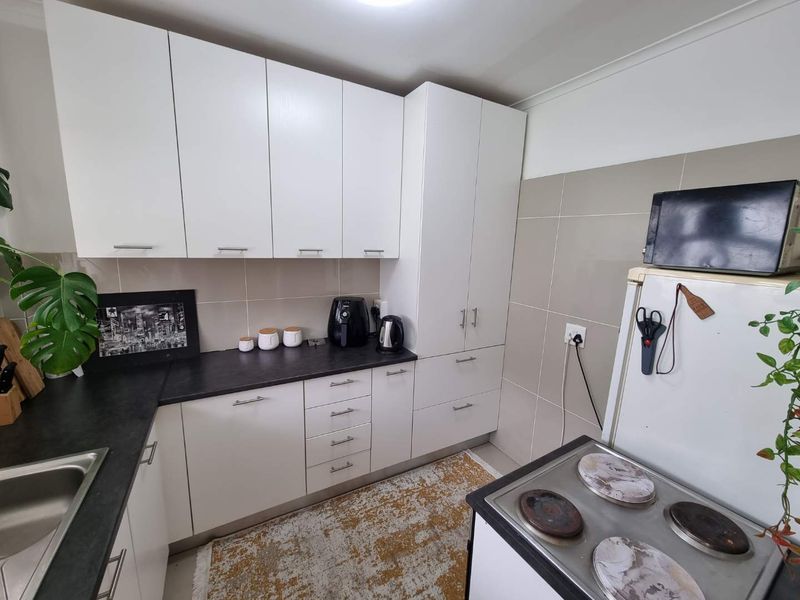 A functional kitchen featuring white cabinetry, dark laminate countertops, a tiled backsplash, and an integrated electric stove.