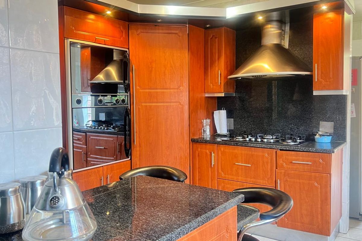 A functional kitchen featuring wood-finish cabinetry, granite countertops, a built-in oven, and a stainless steel extractor fan.