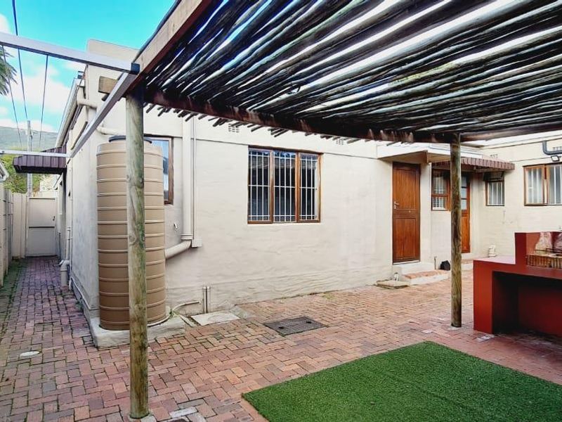 Rear courtyard featuring a paved area, pergola, built-in braai, and a water tank, providing a functional outdoor space.