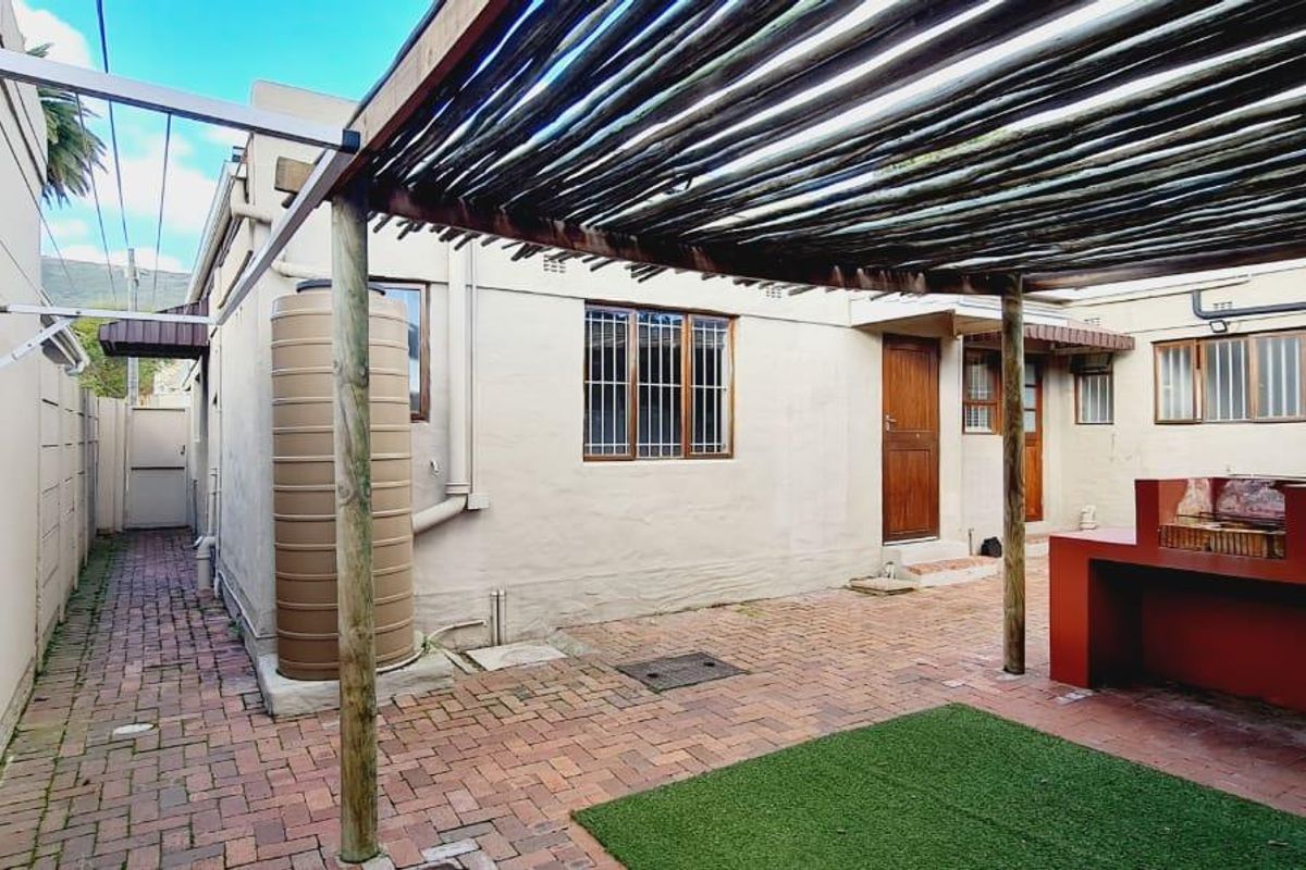 Rear courtyard featuring a paved area, pergola, built-in braai, and a water tank, providing a functional outdoor space.