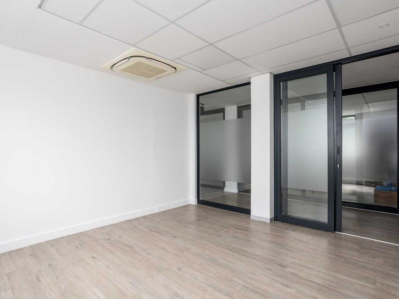 A modern, empty office space featuring laminate flooring, a suspended ceiling with integrated air conditioning, and sleek sliding glass partitions.