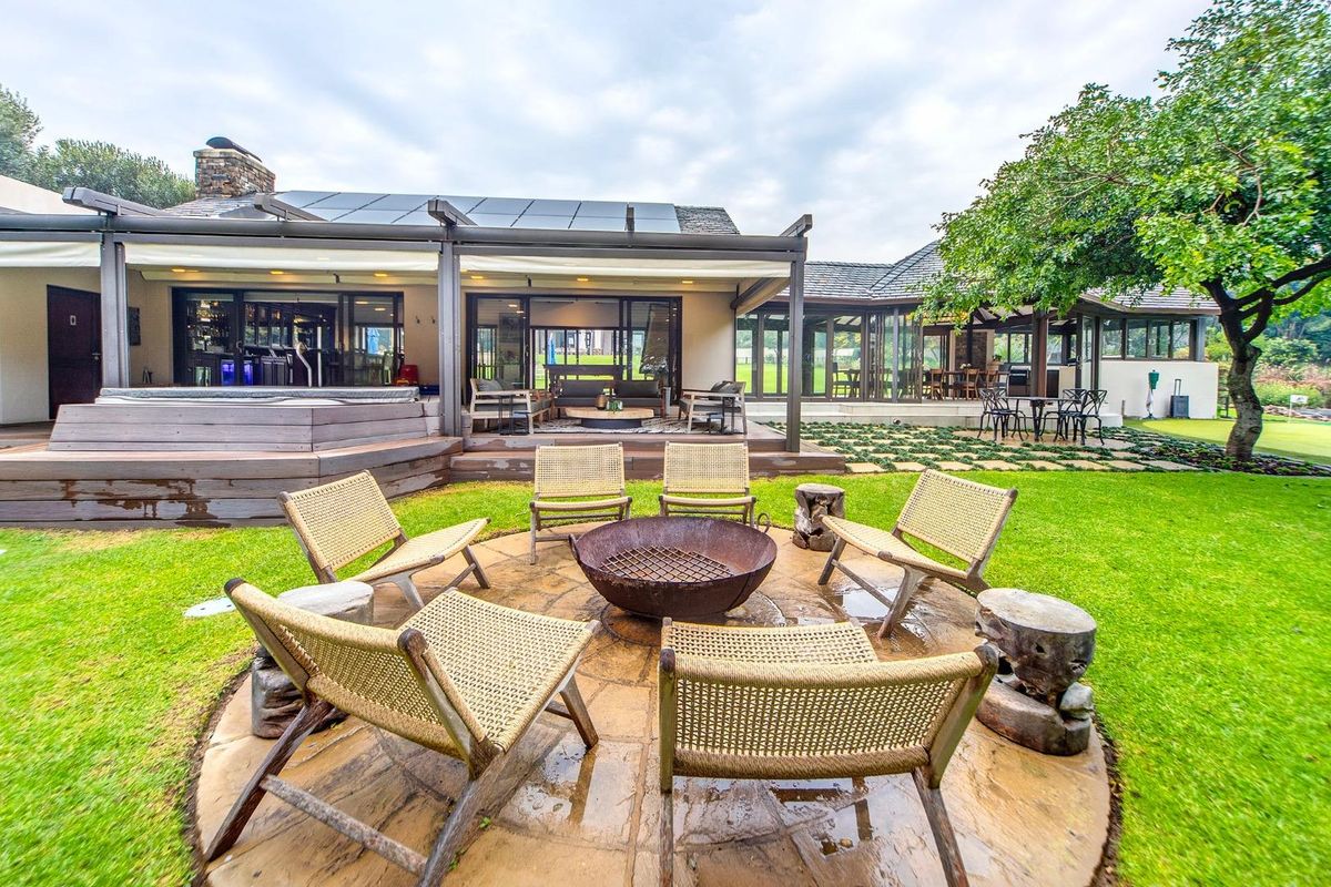 Spacious rear garden featuring a circular stone fire pit area, expansive timber decking, and a covered patio overlooking the landscaped lawn.