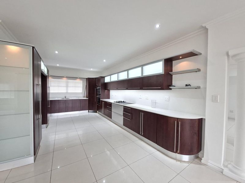 A spacious, modern kitchen featuring dark wood cabinetry, stone countertops, integrated appliances, and sleek porcelain floor tiles with recessed lighting.