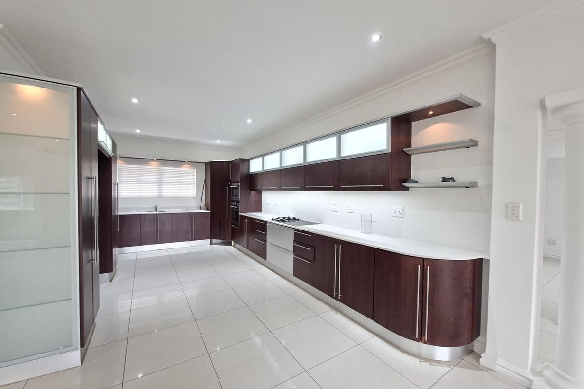 A spacious, modern kitchen featuring dark wood cabinetry, stone countertops, integrated appliances, and sleek porcelain floor tiles with recessed lighting.