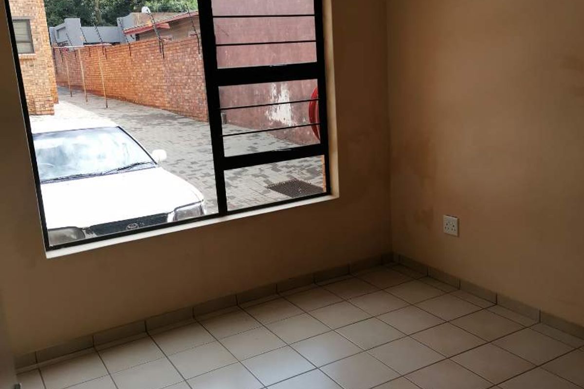 An empty bedroom featuring tiled flooring and a large aluminium-framed window, showing signs of wear on the walls.