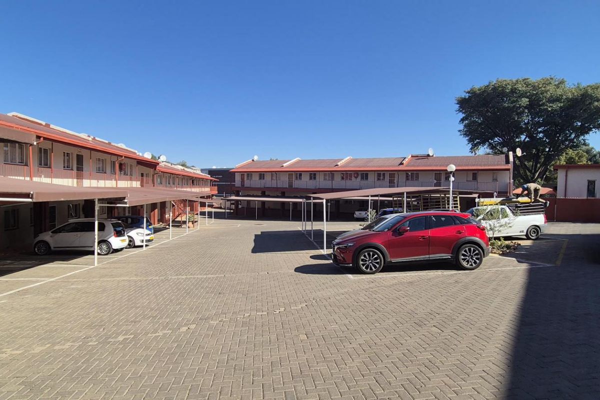 Exterior view of an apartment complex courtyard featuring paved parking areas with covered carports and multi-level residential units.