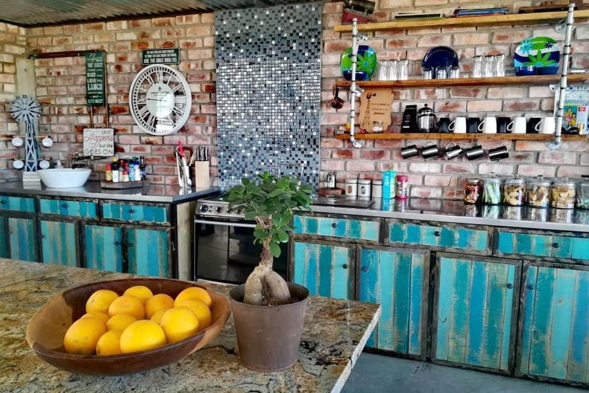 Rustic kitchen area featuring exposed brick walls, custom distressed blue cabinetry, granite countertops, and industrial-style open shelving with a corrugated metal ceiling.