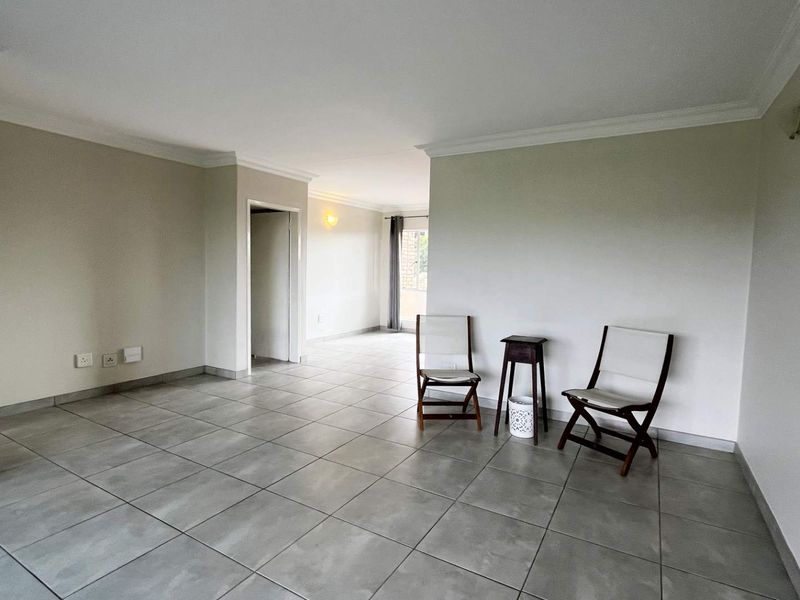 A spacious, open-plan living area featuring neutral wall tones, modern grey floor tiles, and decorative cove cornicing throughout the space.
