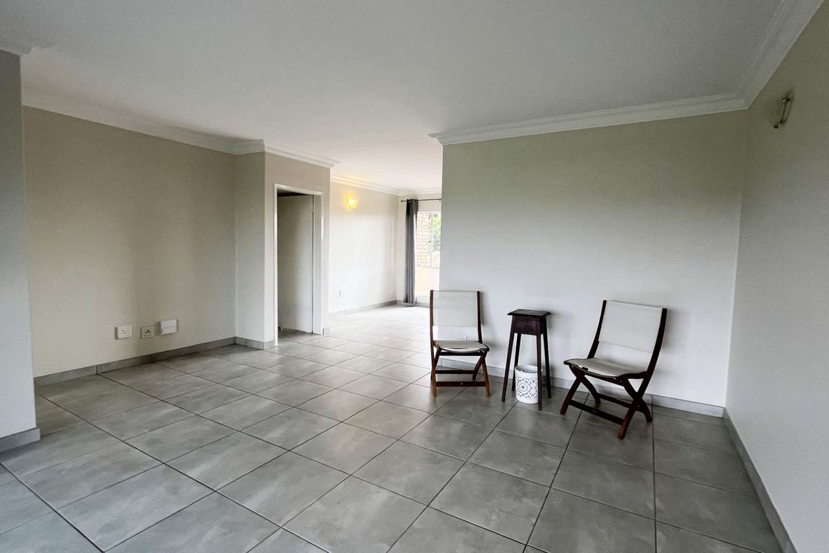 A spacious, open-plan living area featuring neutral wall tones, modern grey floor tiles, and decorative cove cornicing throughout the space.