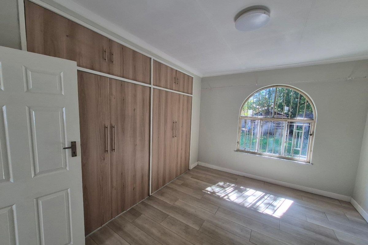 A bright bedroom featuring modern wood-look laminate flooring, built-in floor-to-ceiling wardrobes, and a distinctive arched window.