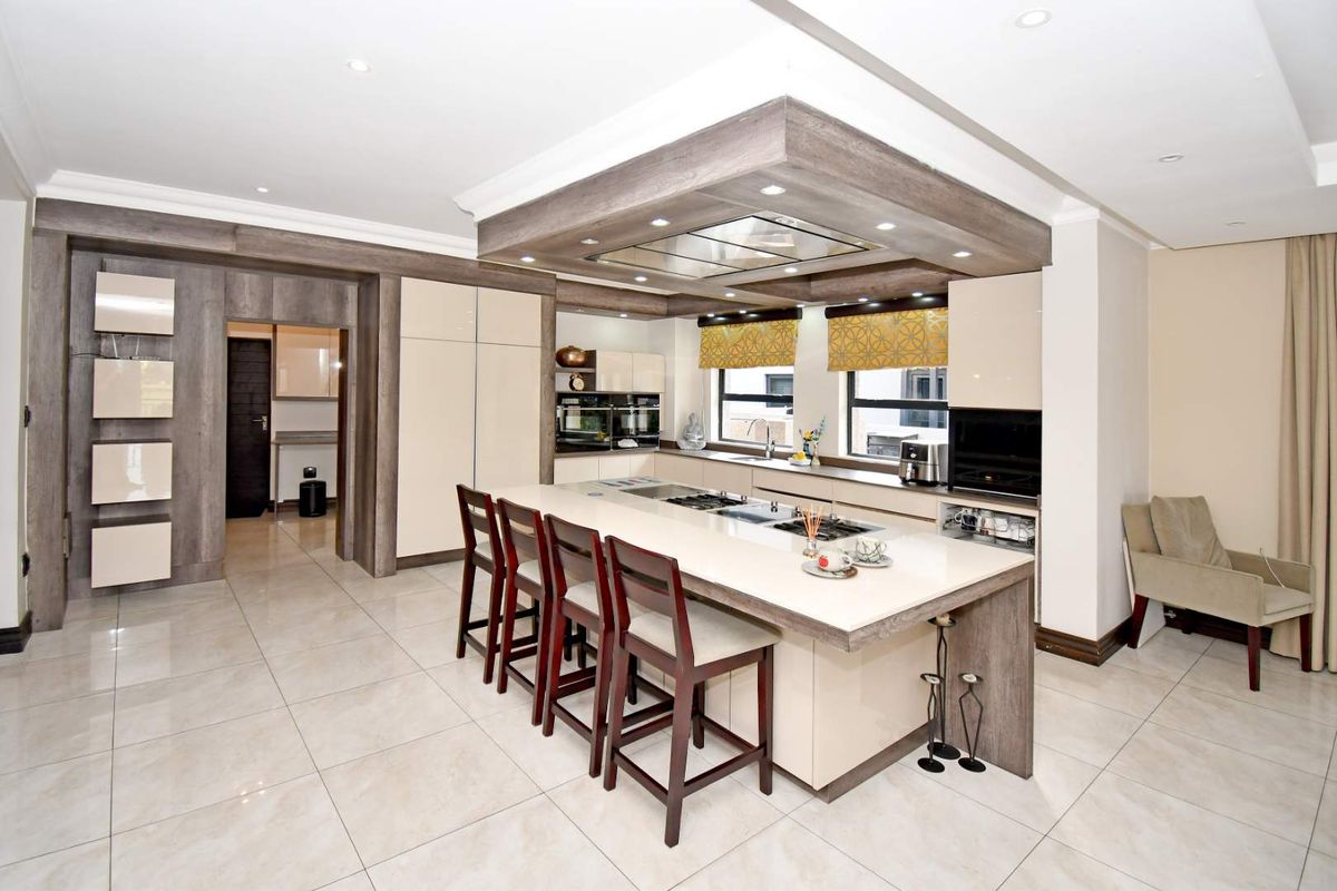 Modern kitchen featuring a large central island with integrated hob, sleek cabinetry, built-in ovens, and recessed ceiling lighting.