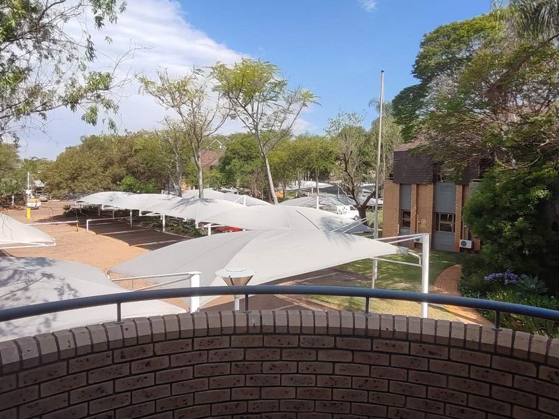 Elevated view from a brick balcony overlooking the office complex grounds, featuring paved parking areas with shade cloth structures and established garden landscaping.