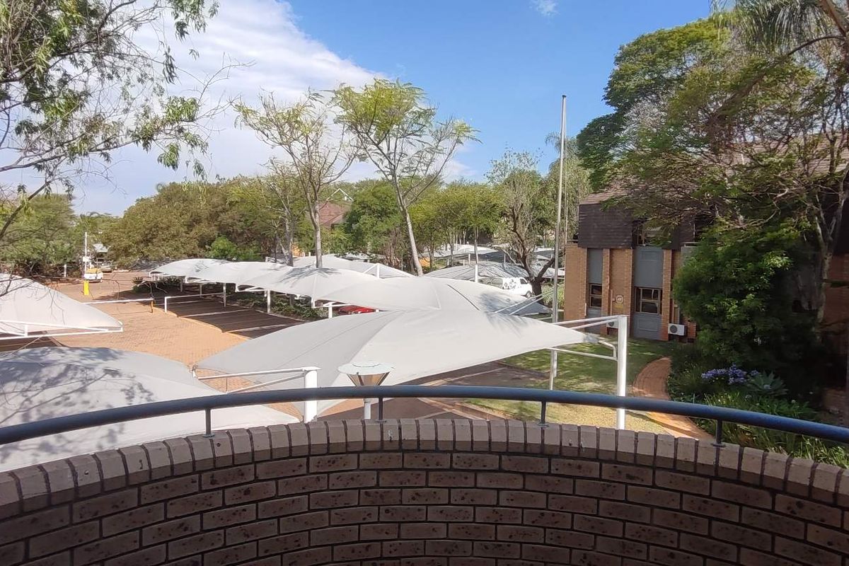 Elevated view from a brick balcony overlooking the office complex grounds, featuring paved parking areas with shade cloth structures and established garden landscaping.