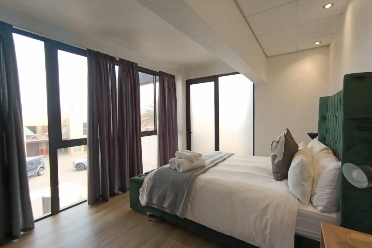 A bright bedroom featuring large floor-to-ceiling windows, laminate flooring, and recessed ceiling lighting, offering a modern and airy atmosphere.