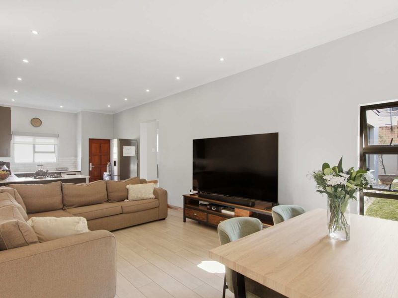 Spacious open-plan living area featuring modern laminate flooring, recessed lighting, and a well-appointed kitchen with subway tile backsplash and integrated cooktop.