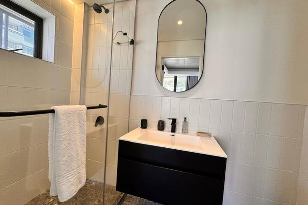 Modern bathroom featuring a floating vanity with black cabinetry, a walk-in shower with glass enclosure, and a contemporary oval wall mirror.